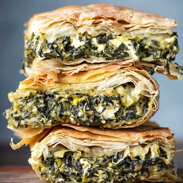 Three stacked slices of spanakopita, revealing flaky phyllo pastry and a spinach-feta filling.