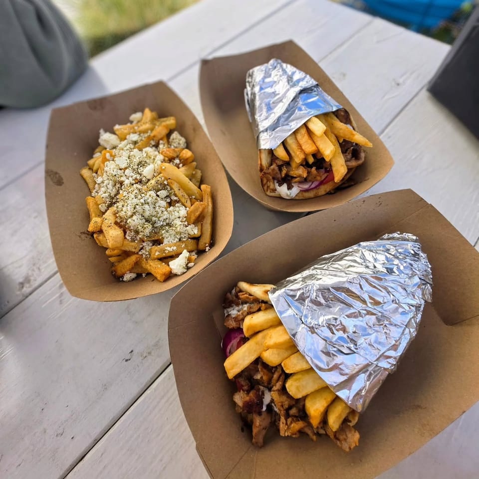 Two Greek gyros with fries and a side of feta fries on a white wooden table.