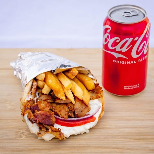 A Greek gyros with fries, meat, and sauce, wrapped in foil, next to a Coca-Cola can.