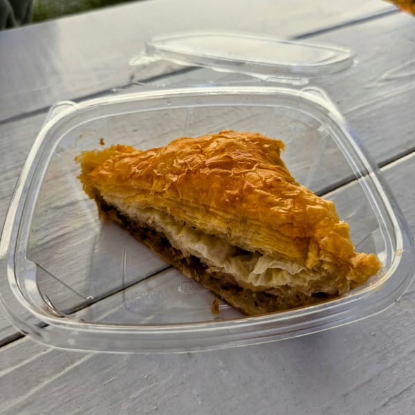 A triangular piece of baklava with flaky layers and a nut filling in a clear plastic container.